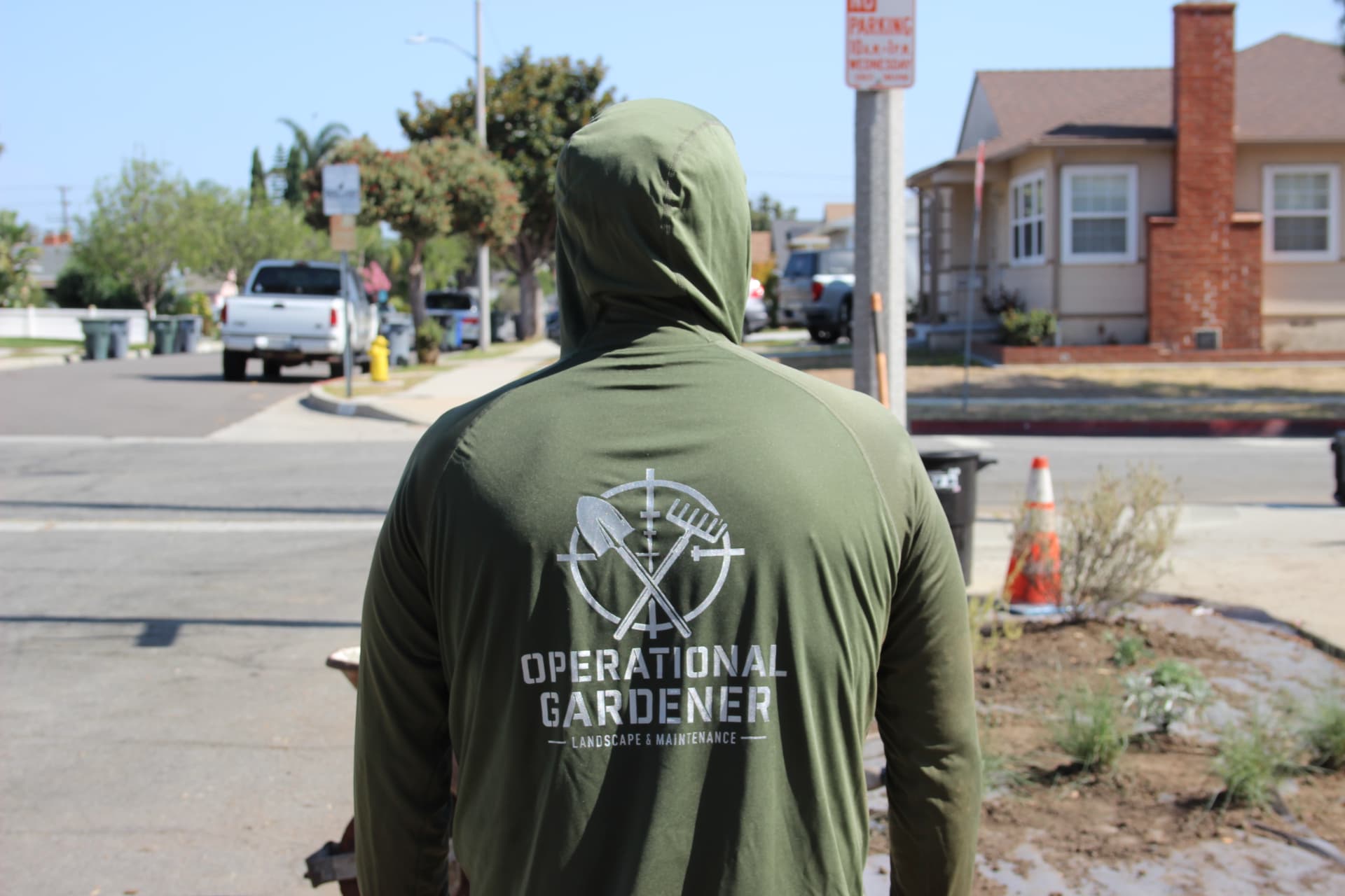 Crew member in an Operational Gardener hoodie working a residential corner lot